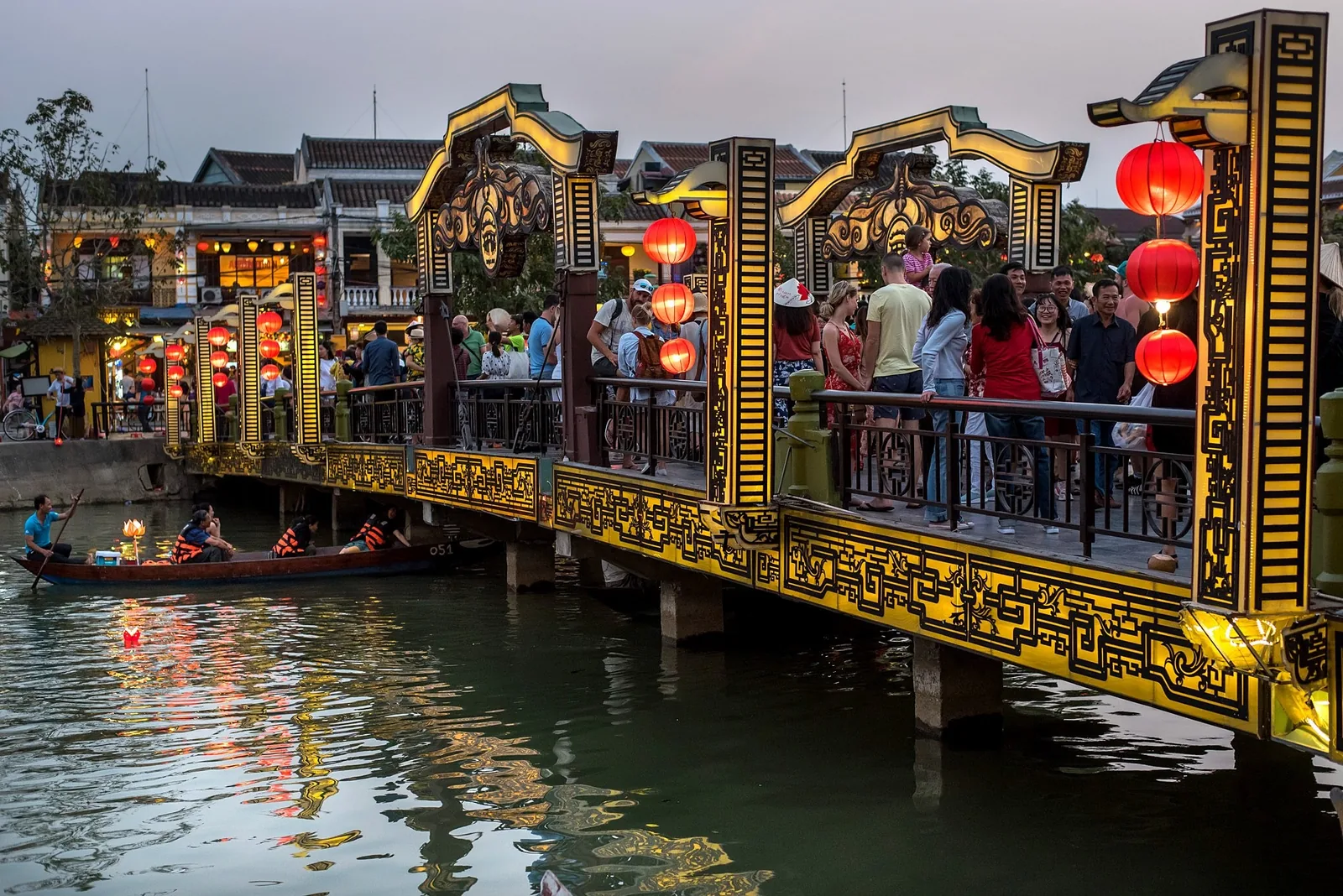 Crowds crossing a lantern-decorated bridge over the river in Hoi An