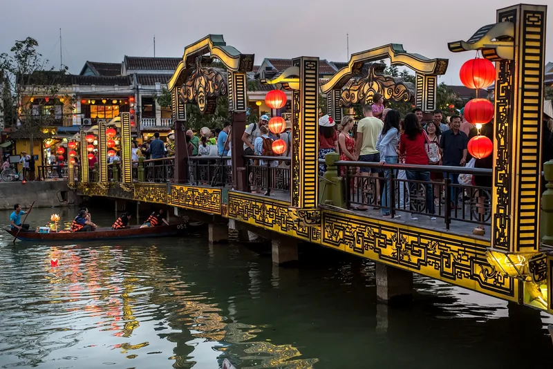 Crowds crossing a lantern-decorated bridge over the river in Hoi An