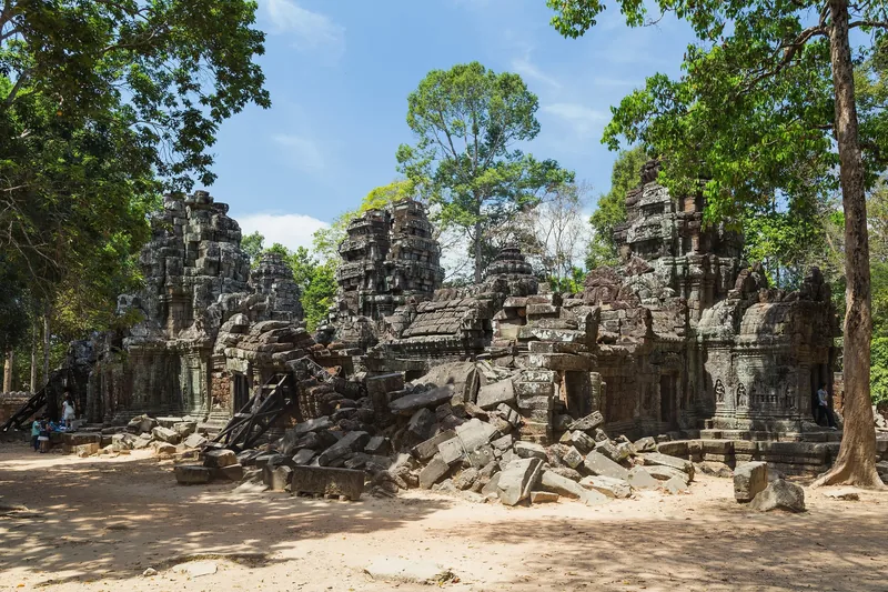 Weathered stone towers and collapsed masonry sit amid tall trees at Ta Som temple in Angkor, Siem Reap.