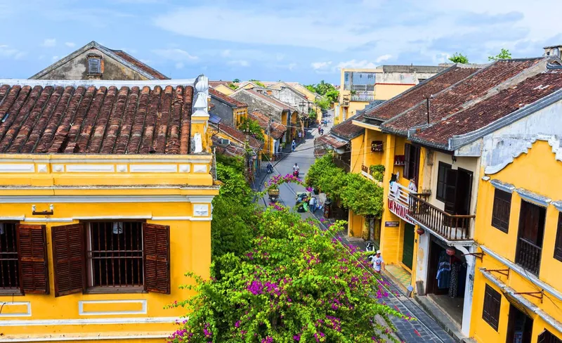 Aerial view of yellow heritage houses with terracotta roofs lining a street in Hoi An's ancient town.