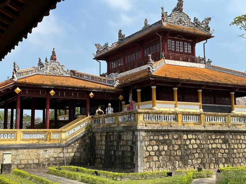 A two-tiered pavilion with ornate red and gold roofs rises above stone walls inside Hue's Imperial City.