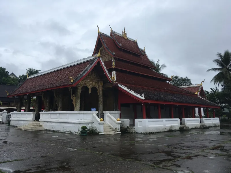 Multi-tiered red roofs of Wat Mai temple stand under a cloudy sky in Luang Prabang.