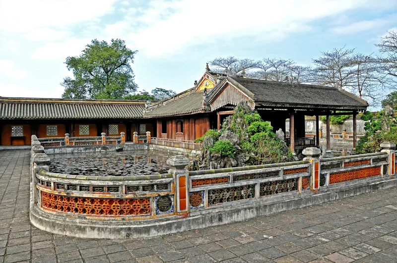 A round pond framed by an ornate stone balustrade sits before wooden pavilions inside Hue's imperial citadel complex.
