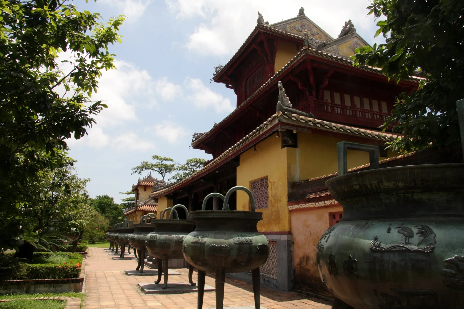 Bronze urns line a pathway beside a yellow imperial pavilion inside Hue's Imperial City.