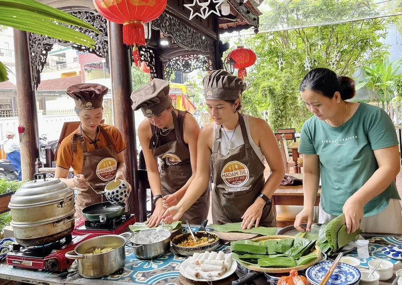 Guests wearing chef hats prepare dishes with banana leaves during a cooking class in Hue.
