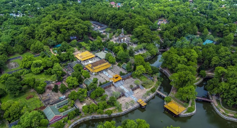 Aerial view of Tu Duc Tomb's yellow-roofed pavilions surrounded by lush greenery and a winding lake in Hue.