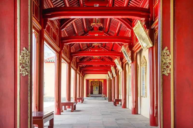 A red and gold lacquered corridor with ornate wooden beams stretches through the Hue Imperial City.