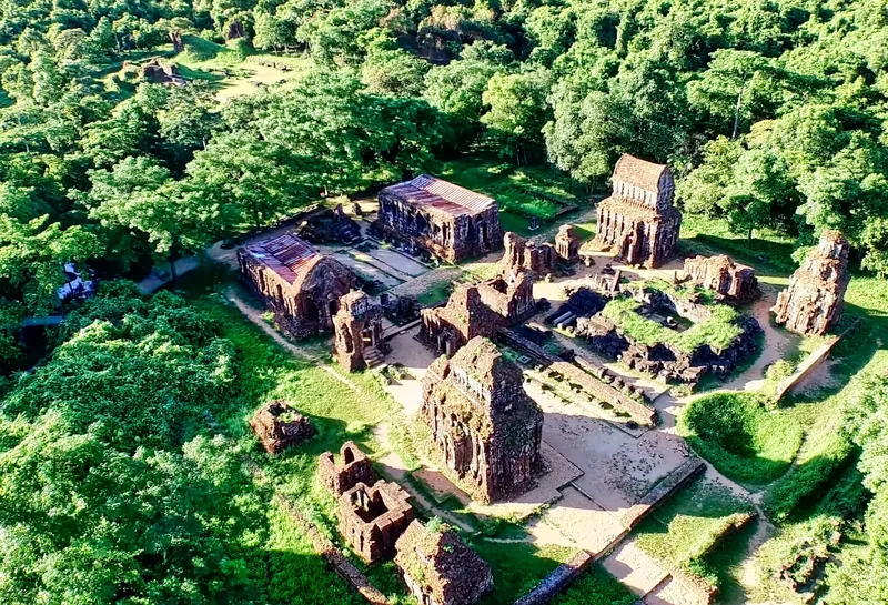 Aerial view of ancient brick Cham towers scattered among lush jungle at My Son sanctuary.