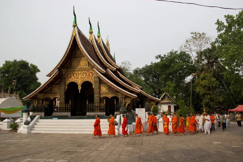 Monks in saffron robes walking past a temple wall in Luang Prabang in early morning