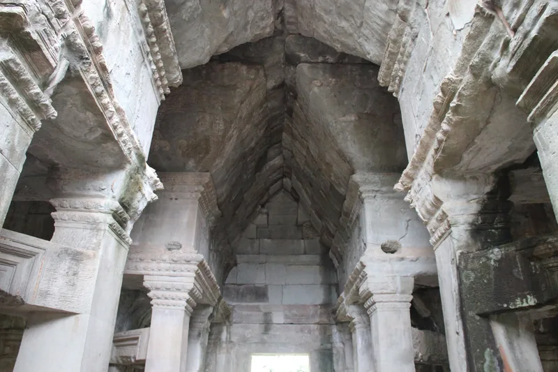 Carved stone columns and a vaulted stone roof line a gallery inside an Angkor temple in Siem Reap.