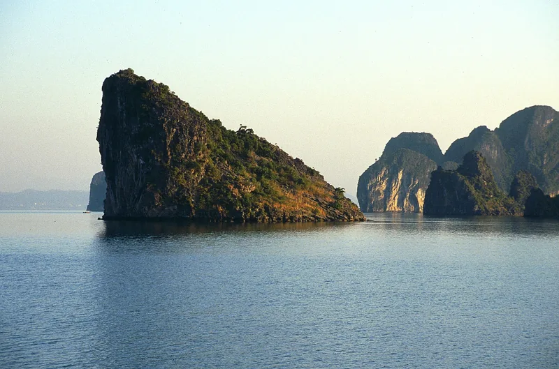 Limestone karst islands rise from calm waters in Ha Long Bay under a soft evening sky.