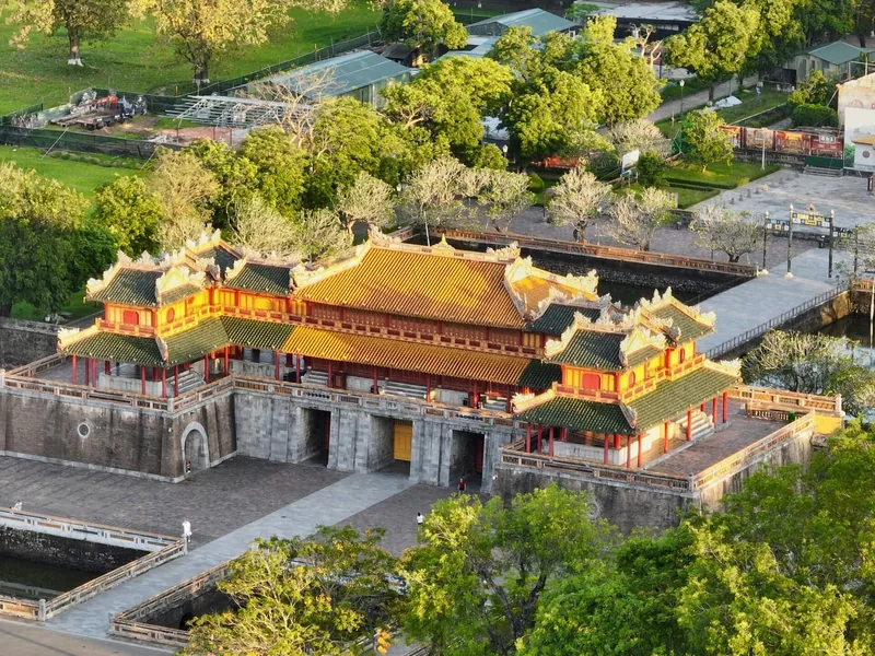 Aerial view of the ornate golden-roofed gate of the Hue Imperial City surrounded by lush green trees.